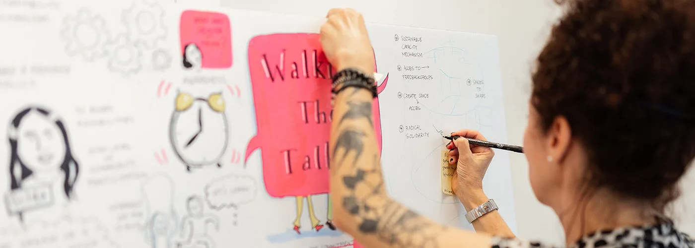 A person taking visual notes. In their drawing te thext "Wlaking the Talk" is visible.